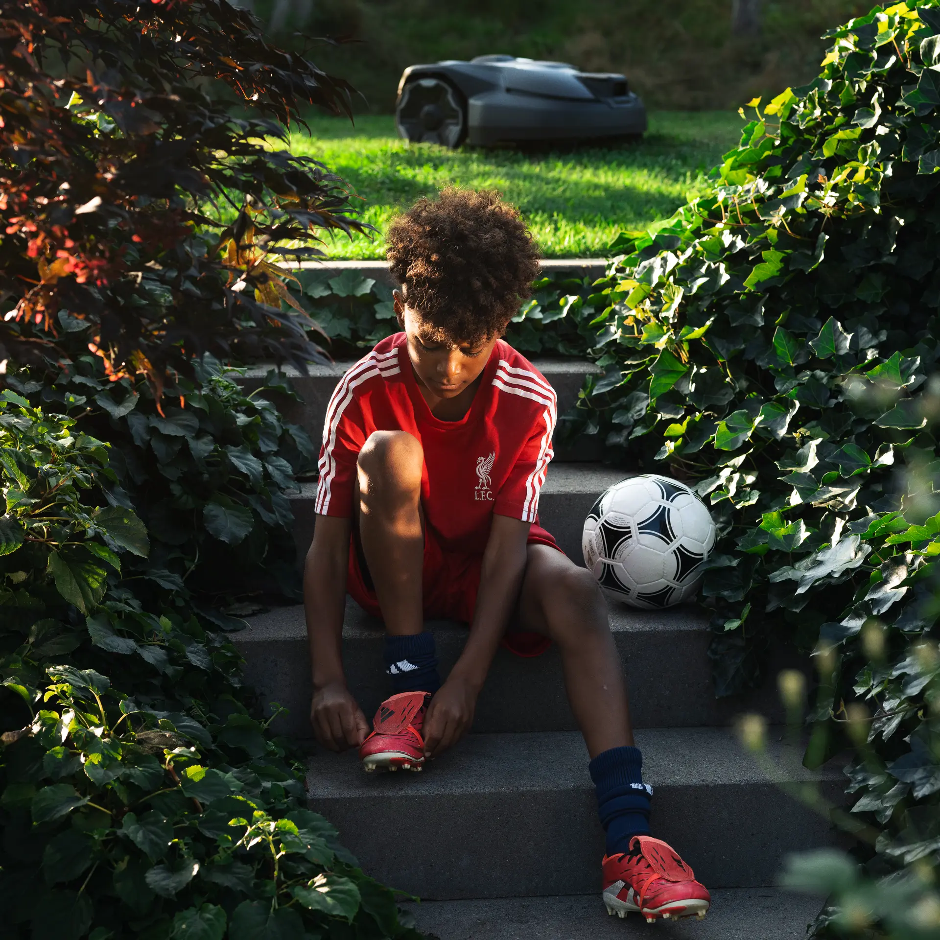 Young Liverpool FC fan lacing his boots in a backyard