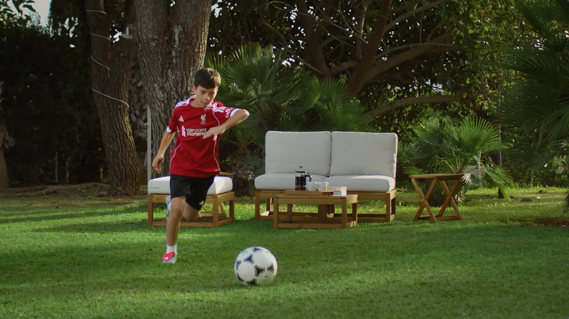 Young Liverpool FC fan playing football in a backyard